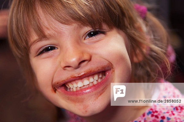 Mädchen lächelt mit Schokolade um den Mund herum