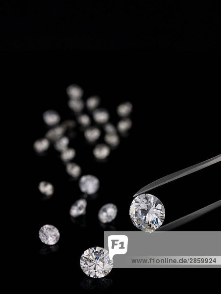 Pinzette und geschliffene Diamanten auf schwarzem Hintergrund