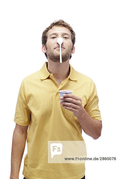 Junger Mann hält Joghurt,  Ausgleichslöffel auf der Nase,  Portrait