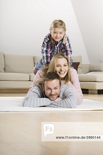 Eltern und Tochter (3-4) entspannt auf Teppich  Portrait