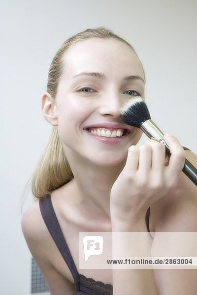 Young woman using make-up brush  smiling  portrait  close-up