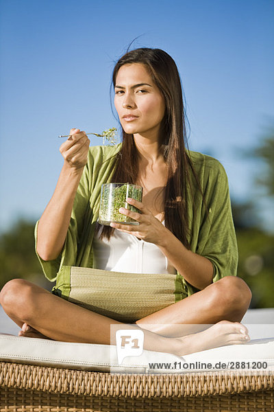 Woman sitting on a mattress and eating bean sprouts