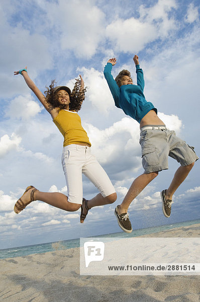 Teenage boy with a girl jumping on the beach
