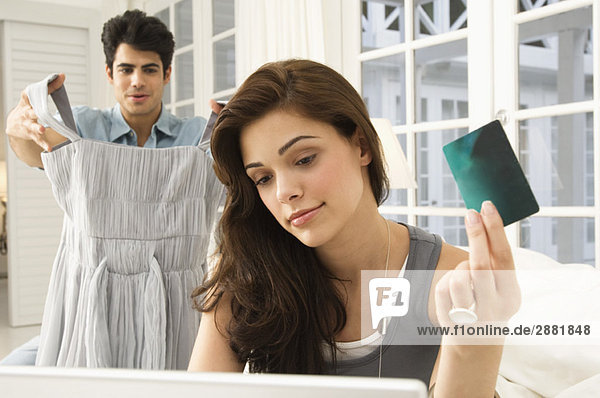 Woman shopping online with a credit card and her husband showing a dress