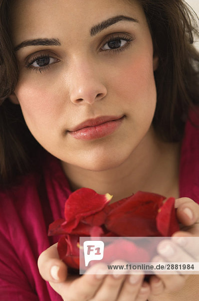 Porträt einer Frau mit einer Handvoll roter Rosenblätter