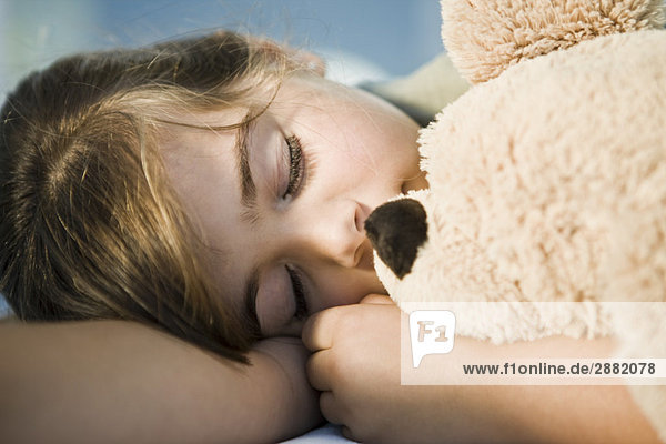 Nahaufnahme eines Mädchens,  das mit einem Teddybären schläft.
