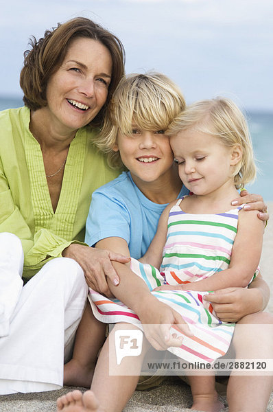 Frau sitzend mit ihren Enkelkindern am Strand