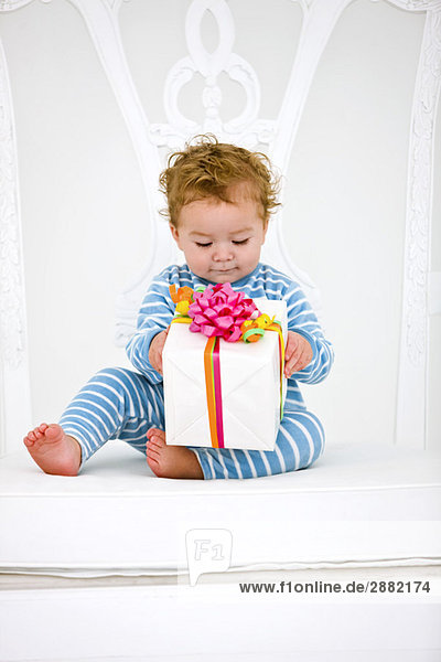Baby boy holding a present in an armchair