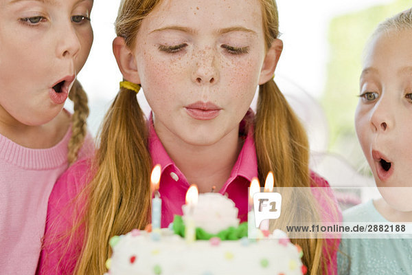 Nahaufnahme von drei Mädchen  die Kerzen auf einer Geburtstagstorte ausblasen.