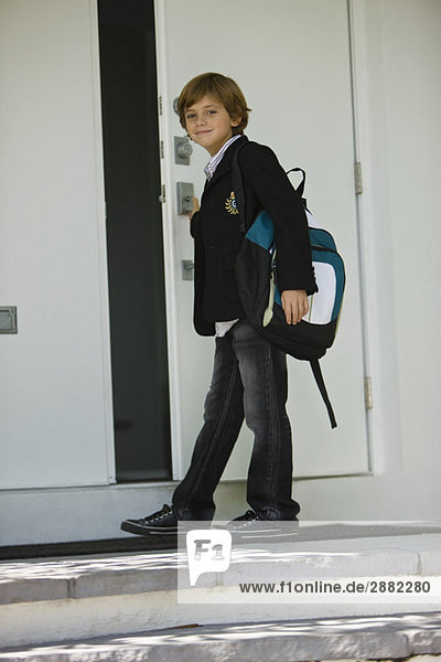 Porträt eines Schuljungen  der die Tür einer Schule öffnet