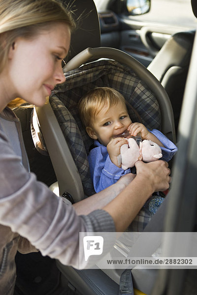 Frau  die ihren Sohn auf einem Kindersitz in einem Auto befestigt.