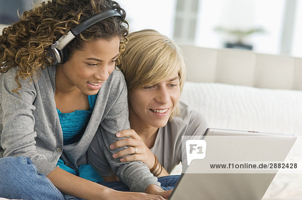 Mädchen hört Kopfhörer und arbeitet an einem Laptop mit einem Teenager neben ihr.
