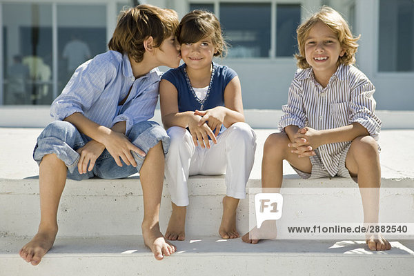 Junge  der ein Mädchen küsst  während sein Freund neben ihnen sitzt.