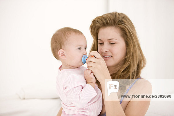 Frau hält einen Schnuller auf dem Mund ihrer Tochter.
