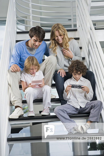 Eltern sitzen mit ihren Kindern auf der Treppe und spielen Videospiele.