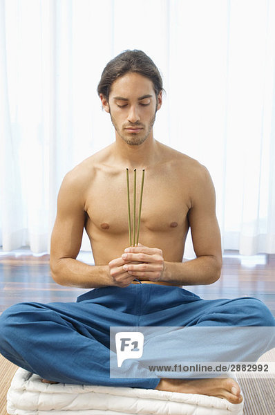 Mann  der Yoga praktiziert und Räucherstäbchen hält.