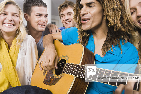 Mann sitzt mit seinen Freunden und spielt Gitarre.