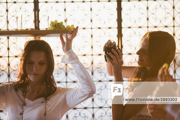 Woman taking a picture of her friend carrying a fruit tray