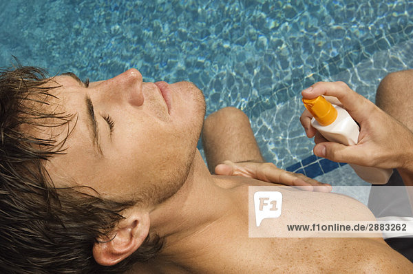 Mann  der Sonnencreme auf seinen Körper am Pool aufträgt.