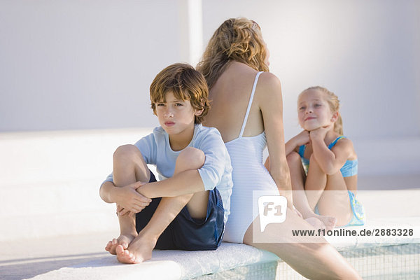 Frau mit ihren beiden Kindern am Pool sitzend