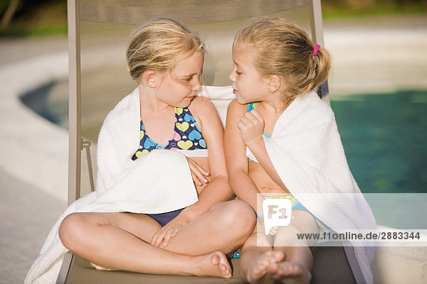 Zwei Mädchen sitzen auf einem Liegestuhl am Pool
