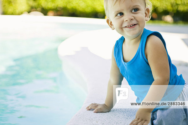 Kleiner Junge  der sich auf die Kante am Pool lehnt.