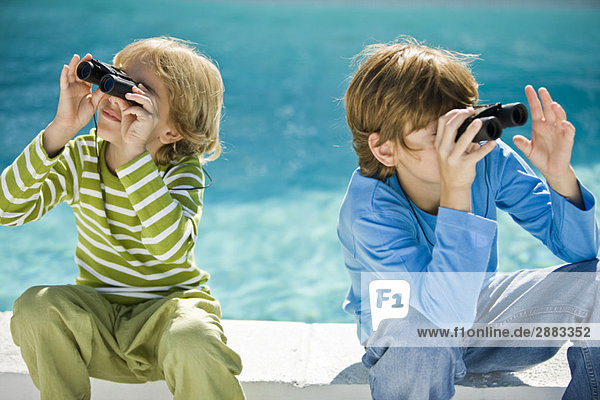 Zwei Jungen  die durch ein Fernglas am Pool schauen.