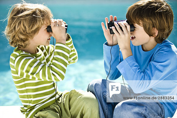 Zwei Jungen sehen sich durch ein Fernglas am Pool an.