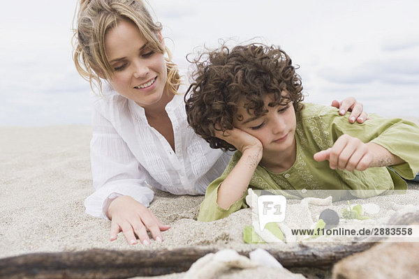 Junge  der mit seiner Mutter am Strand liegt.