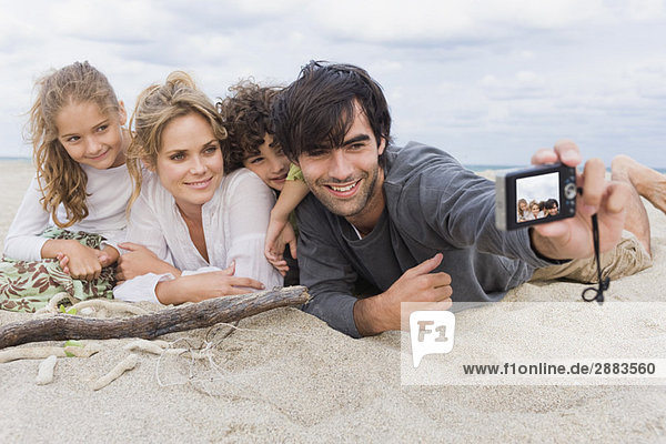 Man taking a picture of his family with a digital camera on the beach