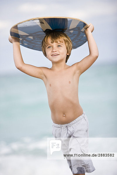 Junge hält ein Bodyboard über den Kopf.