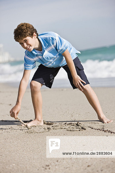 Junge beim Zeichnen im Sand am Strand