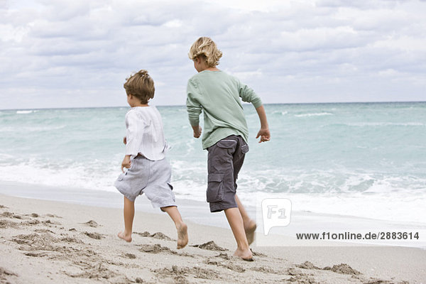 Rear view of two boys running on the beach