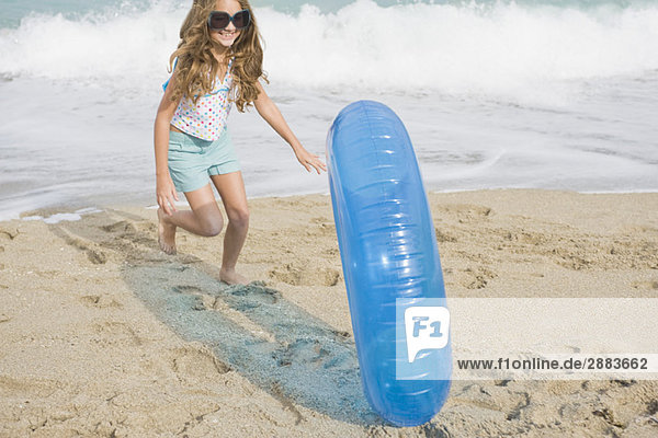 Girl rolling an inflatable ring on the beach
