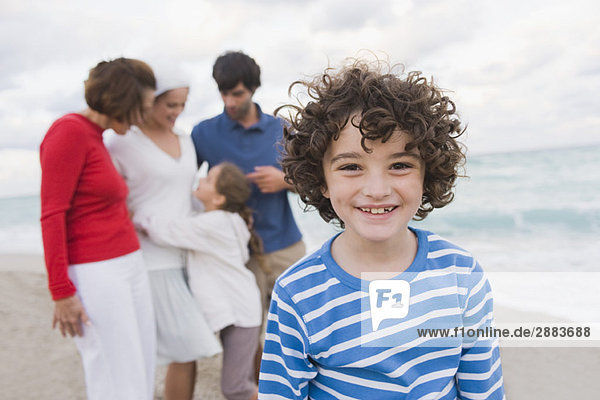 Junge lächelt  seine Familie steht hinter ihm am Strand.