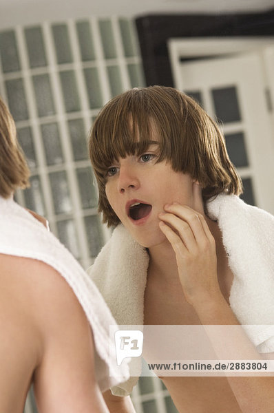 Junge untersucht sein Gesicht im Badezimmerspiegel