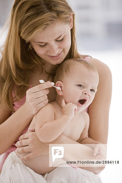 Frau reinigt das Ohr ihrer Tochter mit einem Wattestäbchen
