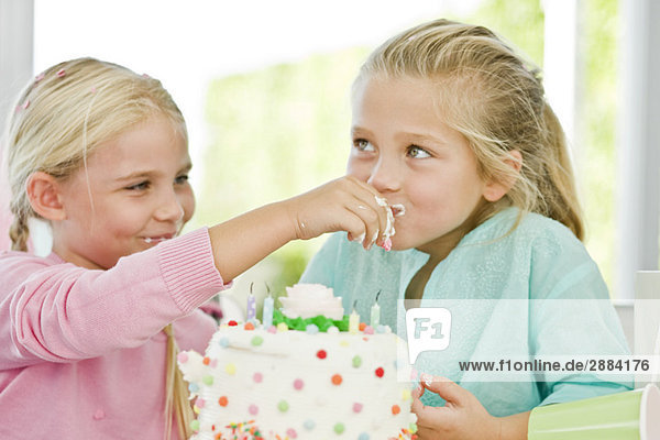 Nahaufnahme eines Mädchens  das seiner Schwester einen Geburtstagskuchen füttert.