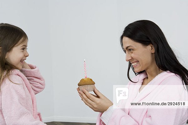 Eine Mutter gibt ihrer Tochter einen Muffin mit einer Kerze darin.