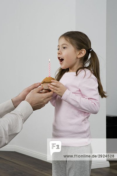 Ein junges Mädchen  das einen Muffin mit einer Geburtstagskerze in sich trägt.