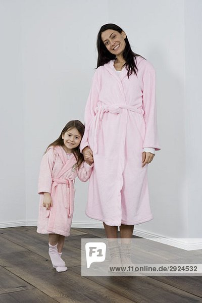 A mother and daughter wearing pink bathrobes holding hands