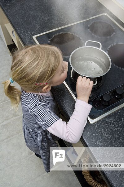 A young girl grabbing a pot of boiling water