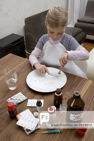A young girl cutting a pill surrounded by medicines