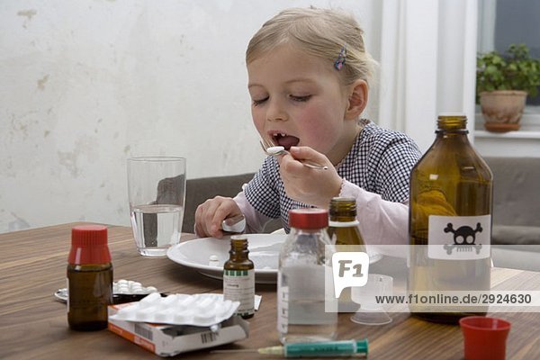 A young girl eating a pill surrounded by medicines