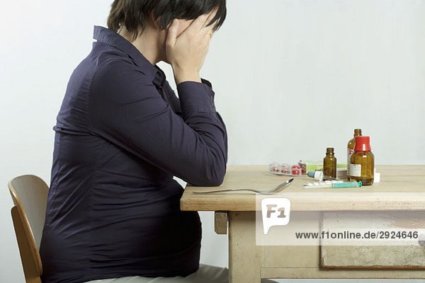 A pregnant woman sitting at a table filled with drugs