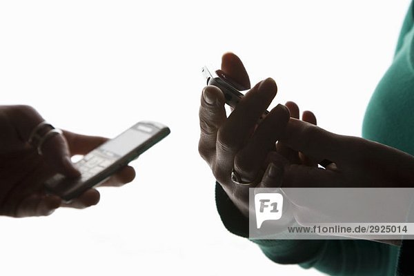 Die Hände von zwei Personen  die Mobiltelefone benutzen.