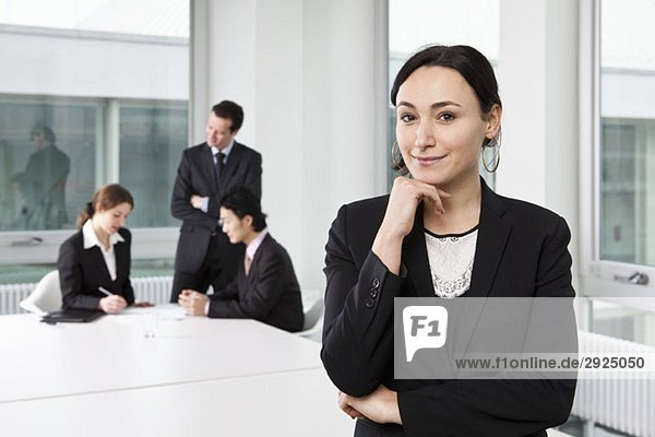Porträt einer Geschäftsfrau in einem Vorstandszimmer mit unscharfen Geschäftsleuten im Hintergrund