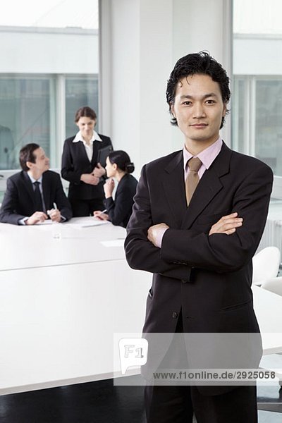 Porträt eines Geschäftsmannes in einem Vorstandszimmer mit unscharfen Geschäftsleuten im Hintergrund