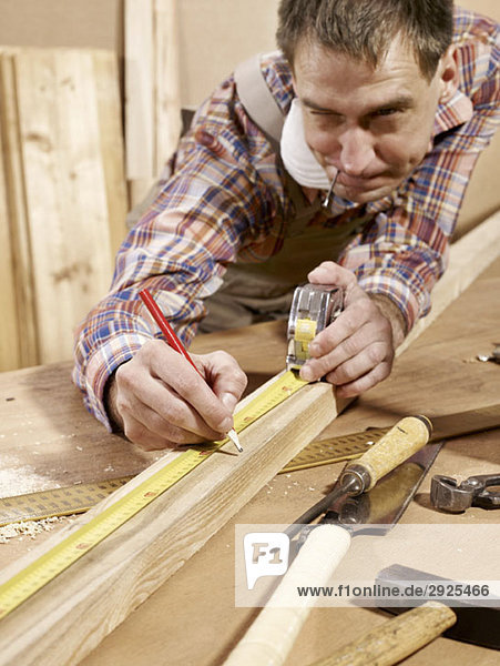 Man marking piece of timber using pencil and tape measure