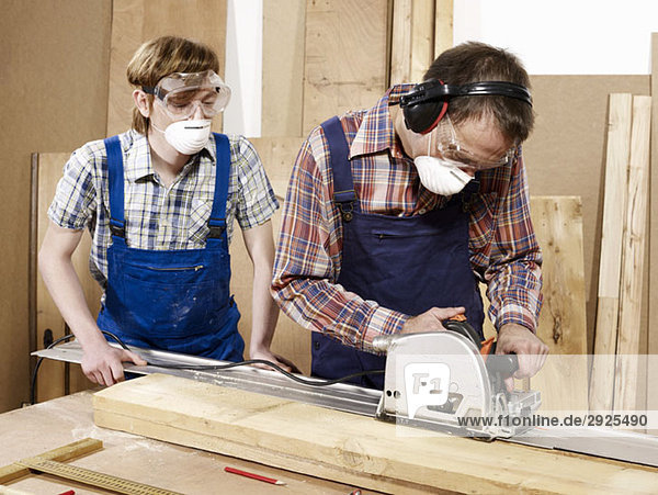 Two men cutting wood in a workshop